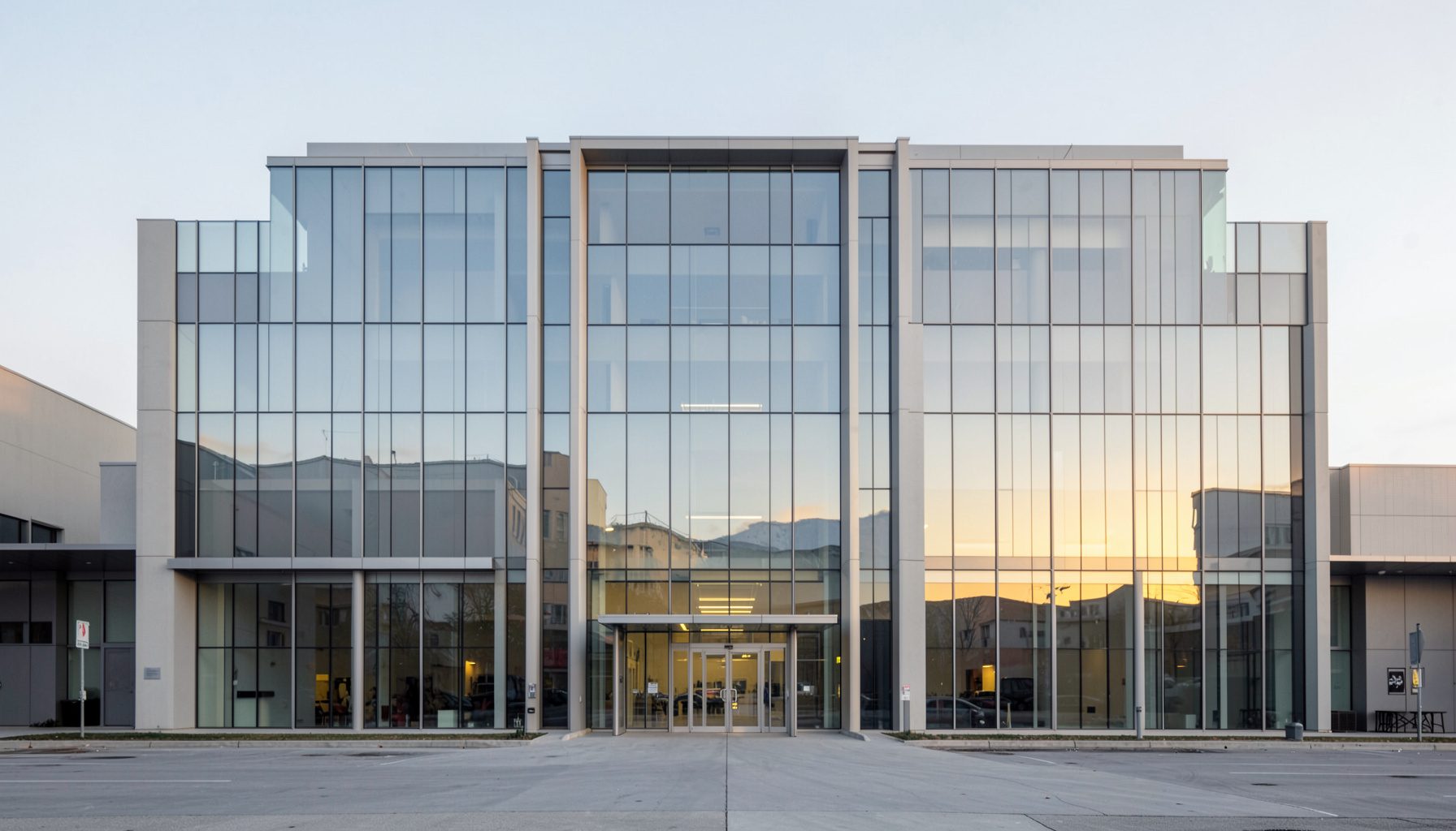 Clean architectural photograph of a modern film studio building with strong symmetry, glass facade reflecting soft morning light, muted grays and pale blues