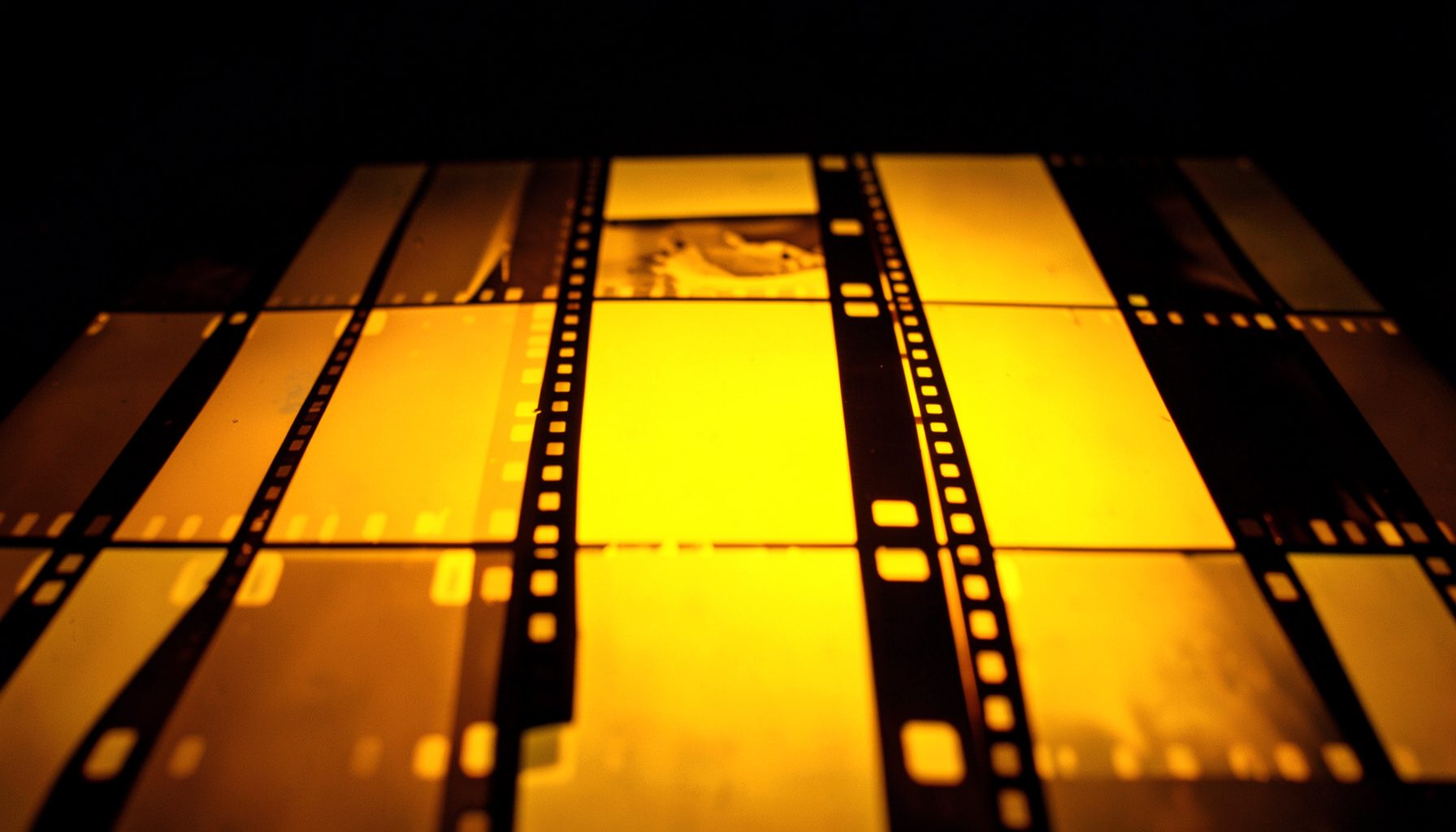 Close-up of 35mm film strips laid across a light table, warm amber glow revealing individual frames, dark background